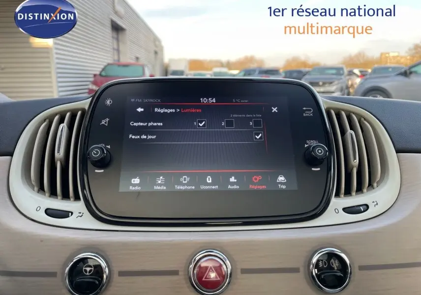 Tableau de bord beige clair de la Fiat 500 blanche 1.0 Hybrid 70CH DolceVita avec écran tactile central affichant les réglages lumières.