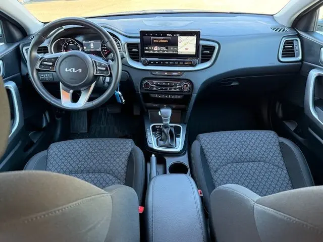 Vue intérieure avant de la Kia CEE'D 2024 avec tableau de bord moderne, écran tactile et sièges tissu gris.