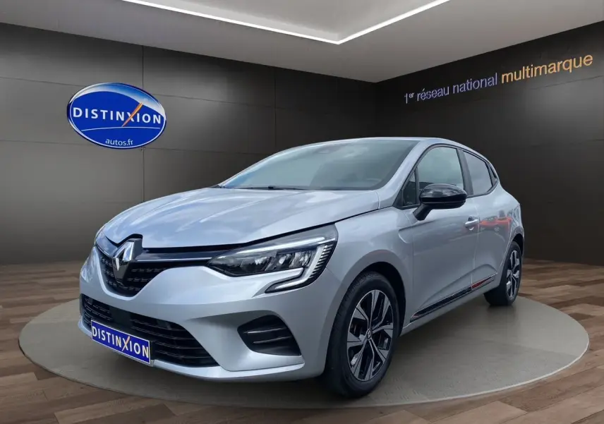 Renault Clio V TCE 90 gris Highland vue 3/4 avant droit, jantes alliage et feux LED distinctifs visibles.