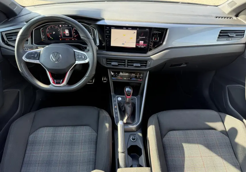 Vue intérieure frontale du tableau de bord et volant cuir GTI de la Volkswagen Polo 2.0 TSI 2024, sièges tissu à carreaux.