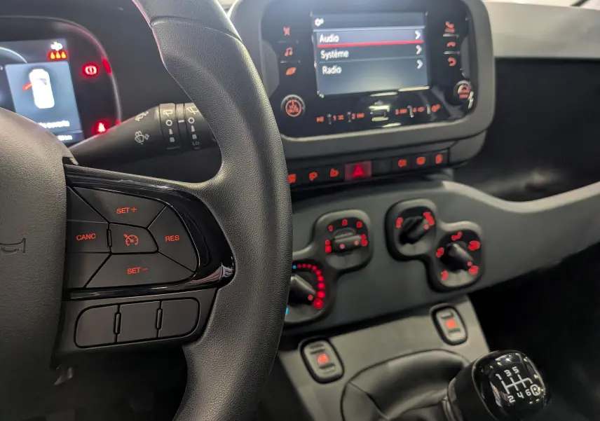 Vue intérieure centrée sur le volant et la console centrale de la Fiat Panda 1.0 Hybrid 2025 avec boîte manuelle et commandes rouges.