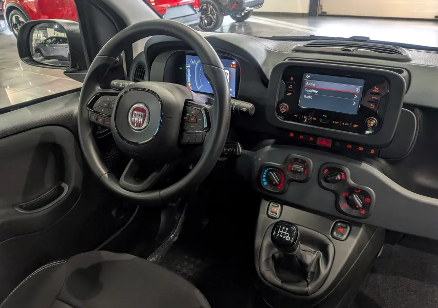 Vue intérieure côté conducteur de la Fiat Panda 1.0 Hybrid 2025, avec tableau de bord noir et écran tactile central allumé.
