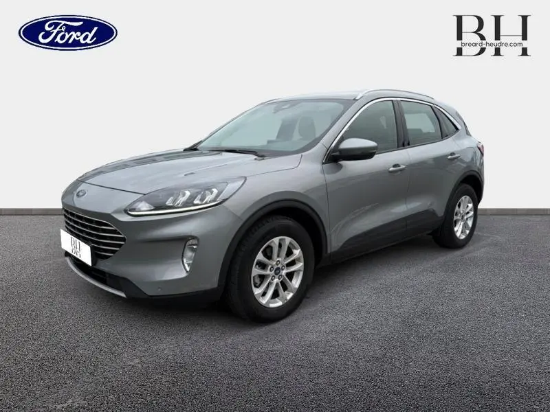 Ford Kuga gris Solar métallisé en vue 3/4 avant droit, avec jantes alu et barres de toit visibles.