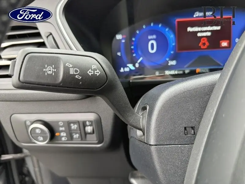 Gros plan sur la commande de clignotants à gauche du volant du Ford Kuga gris Solar, avec tableau de bord digital bleu en arrière-plan.