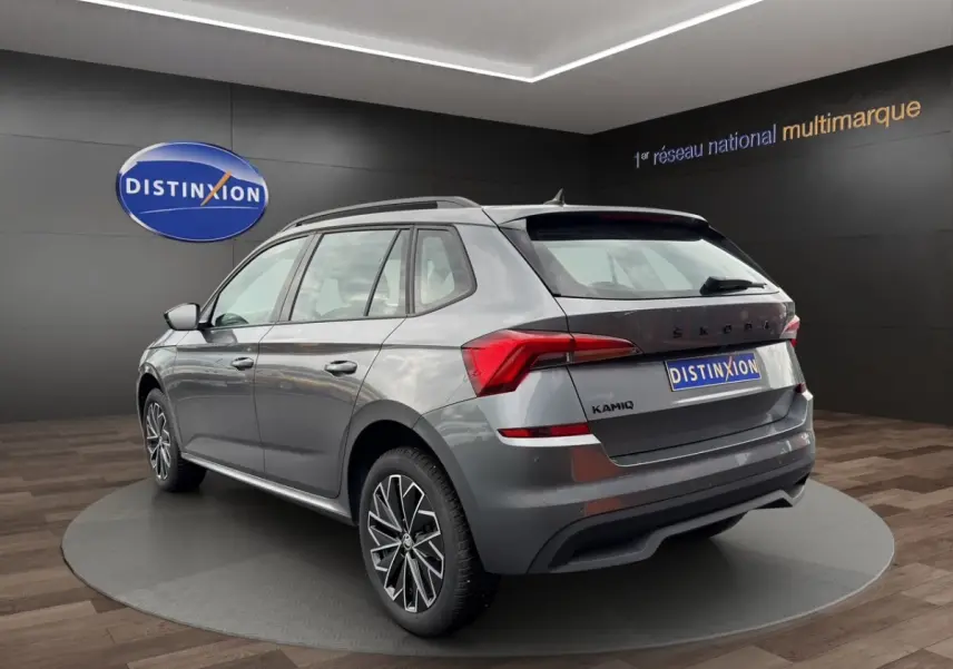 SKODA KAMIQ gris foncé en profil côté gauche, avec jantes bi-ton et toit noir visible en showroom.