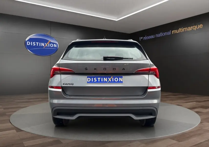Vue 3/4 arrière droite d'un Skoda Kamiq gris foncé avec jantes bi-ton et caméra de recul en showroom.