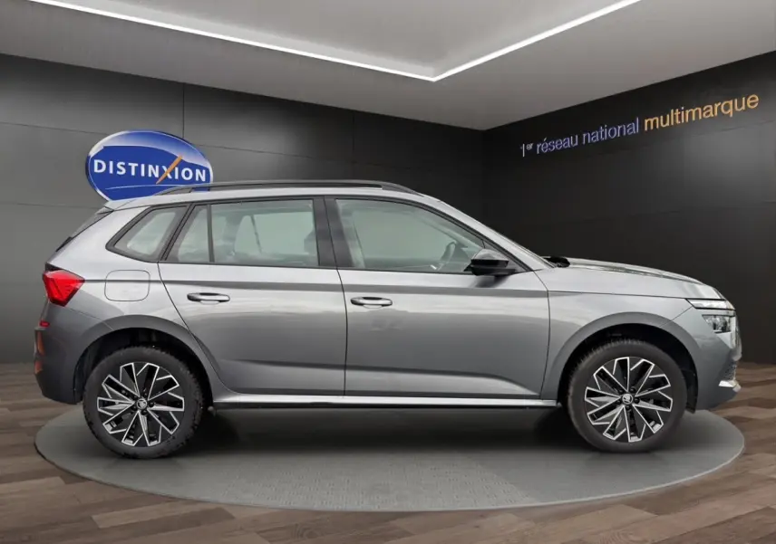 Vue 3/4 arrière droite d'un Skoda Kamiq gris foncé avec jantes bi-ton et caméra de recul en showroom.