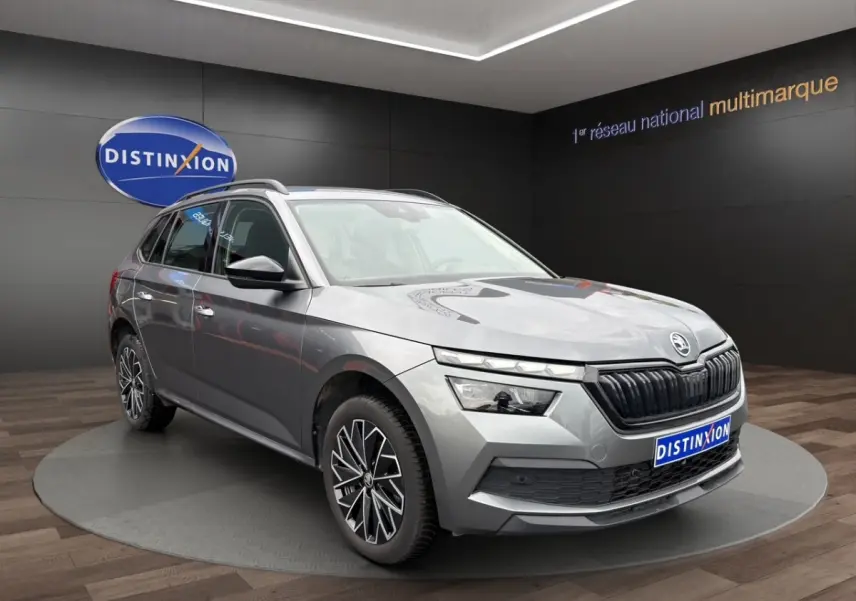 Vue de profil côté gauche d'un Skoda Kamiq gris foncé 2023 avec jantes bi-ton et barres de toit noires.