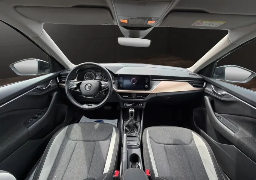 Vue intérieure côté conducteur du Skoda Kamiq gris clair 2023, montrant sièges tissu bicolore et tableau de bord bois clair.