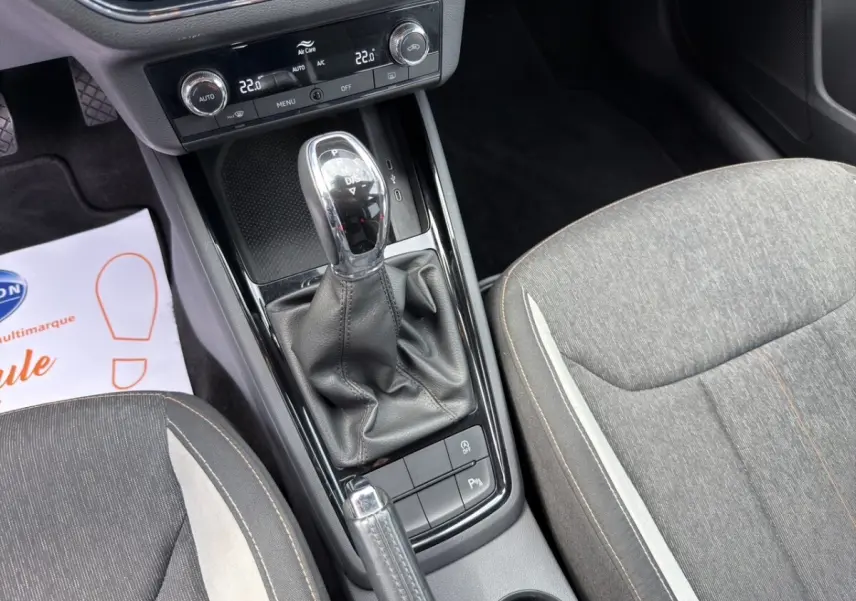 Vue intérieure centrée sur la console centrale avec levier de vitesse automatique et sièges tissu gris du Skoda Kamiq 2023.