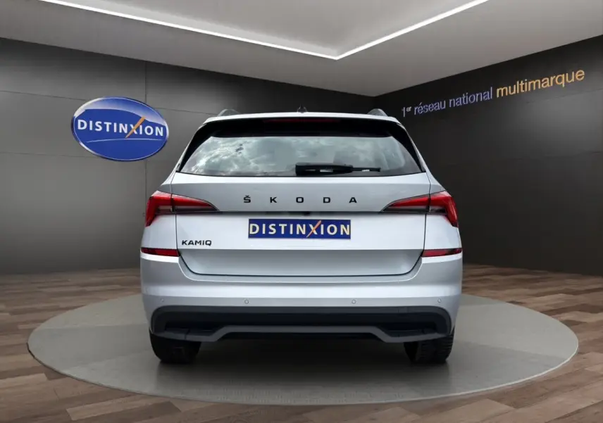 Vue 3/4 arrière droite d'un Skoda Kamiq gris clair avec jantes bi-ton et caméra de recul en showroom.