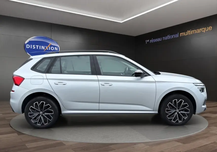 Vue 3/4 arrière droite d’un Skoda Kamiq gris clair avec jantes bi-ton et barres de toit noires.