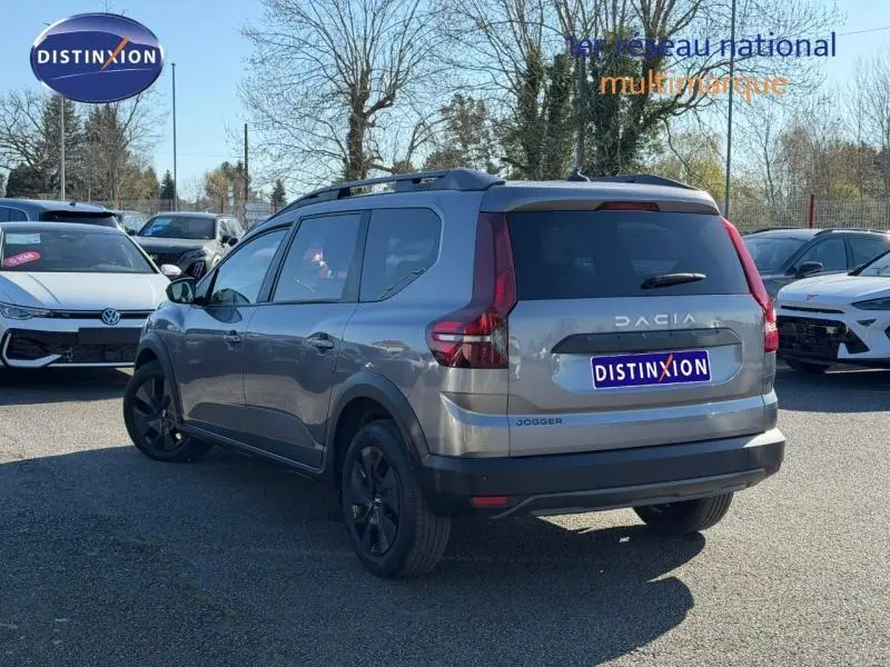 Vue 3/4 arrière droite d'un Dacia Jogger gris schiste métallisé 2025 avec toit noir et barres de toit noires.