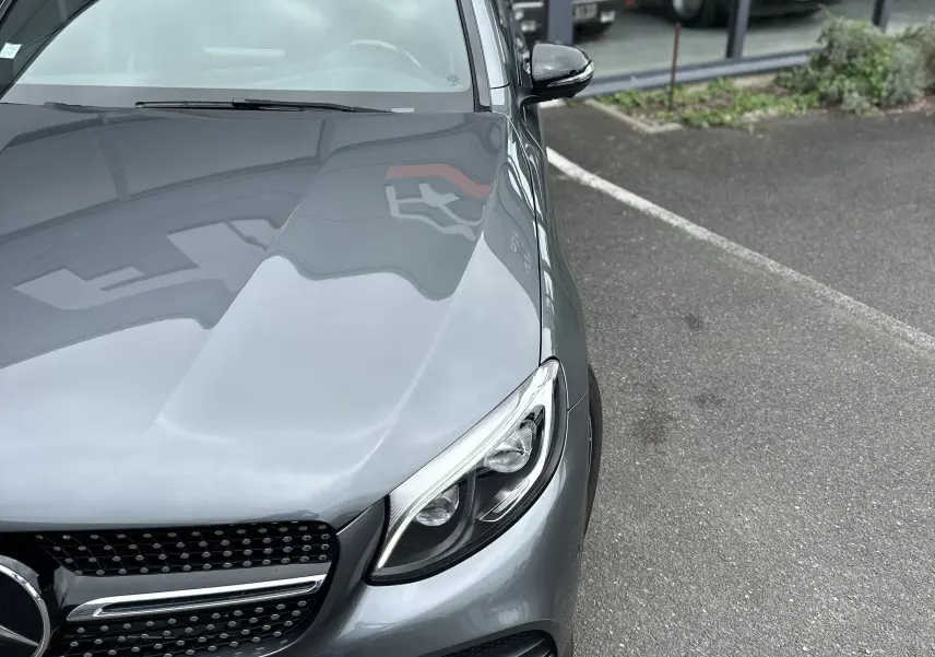 Vue 3/4 avant droit d'un Mercedes GLC Coupé 250 D Fascination gris foncé, avec calandre étoilée et phares LED visibles.