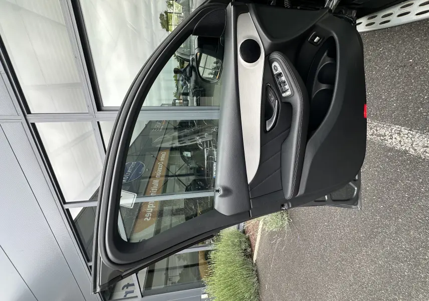 Vue rapprochée de la porte avant gauche ouverte du Mercedes GLC Coupé 250 D Fascination gris foncé, avec garniture noire et insert argenté.