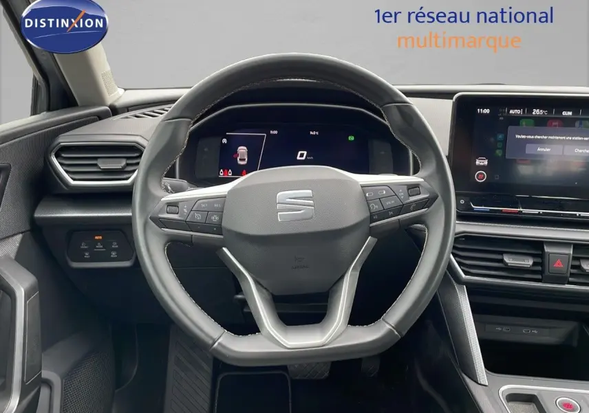 Vue rapprochée du volant et du tableau de bord numérique d'une SEAT LEON ST gris urbain 2023 avec écran tactile central.