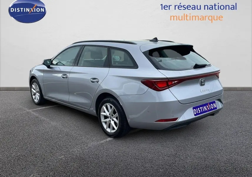 SEAT Leon ST gris urbain vue 3/4 arrière côté gauche, break compact avec feux arrière reliés par un bandeau lumineux.