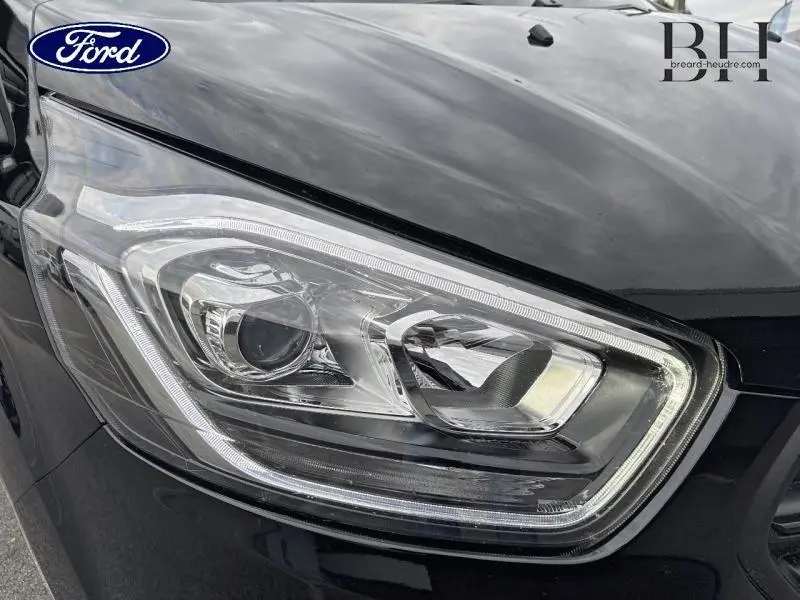Gros plan sur le phare avant droit du Ford Transit Custom noir Agate métallisé, mettant en valeur son design moderne et lumineux.