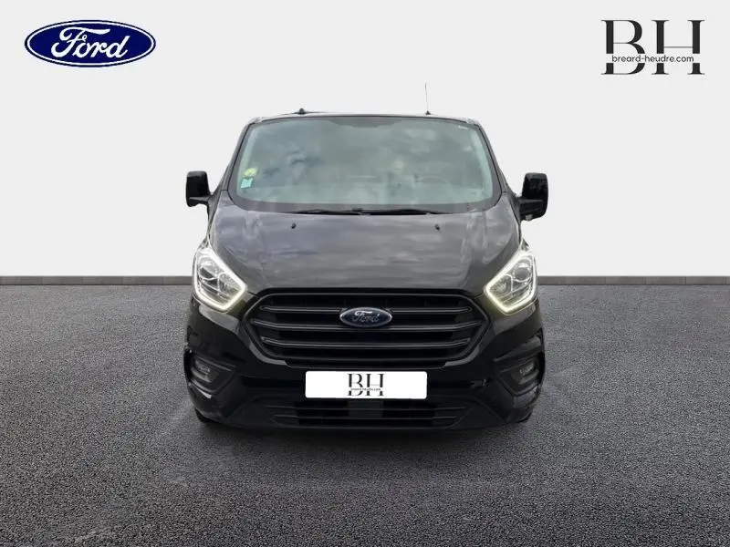 Vue avant d'un Ford Transit Custom noir Agate métallisé avec phares LED allumés sur fond neutre.