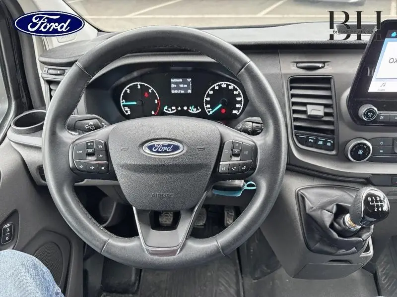 Vue intérieure centrée sur le volant cuir et levier de vitesses manuelle du Ford Transit Custom noir Agate 2023.