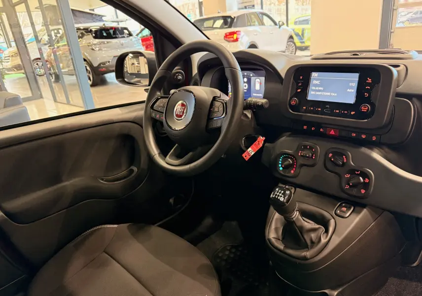 Intérieur de la Fiat Panda 1.0 Hybrid 2025 vu côté conducteur, volant multifonction et levier de vitesses manuel visibles.