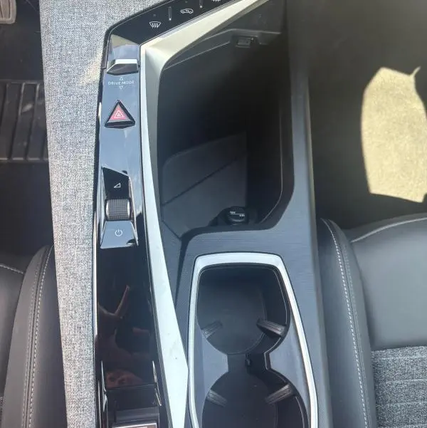 Vue plongeante sur la console centrale grise et noire du Peugeot 3008 Hybrid 136 e-DCS6 Allure 2025 avec commandes tactiles et porte-gobelets.