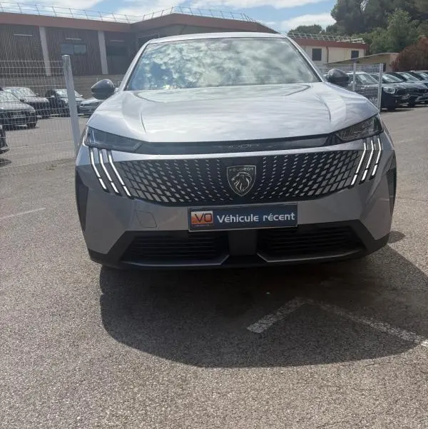 Vue de face du Peugeot 3008 Hybrid gris clair 2025 avec calandre noire et feux LED en forme de griffes.