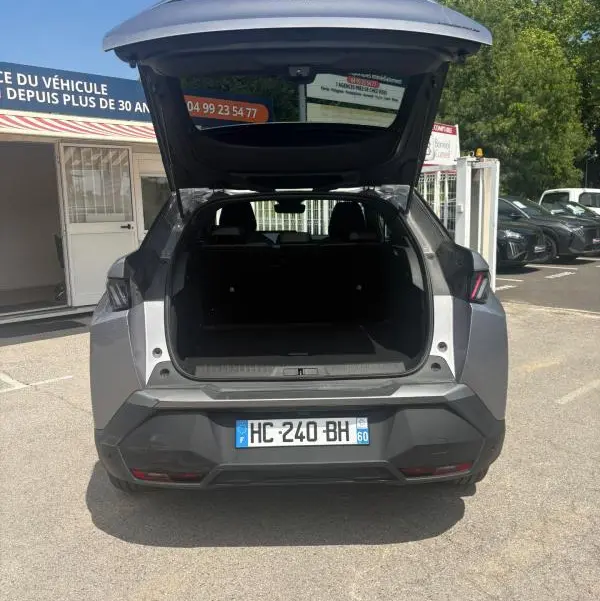 Vue arrière d'un Peugeot 3008 Hybrid gris clair 2025 avec coffre ouvert, montrant l'espace de chargement vide.