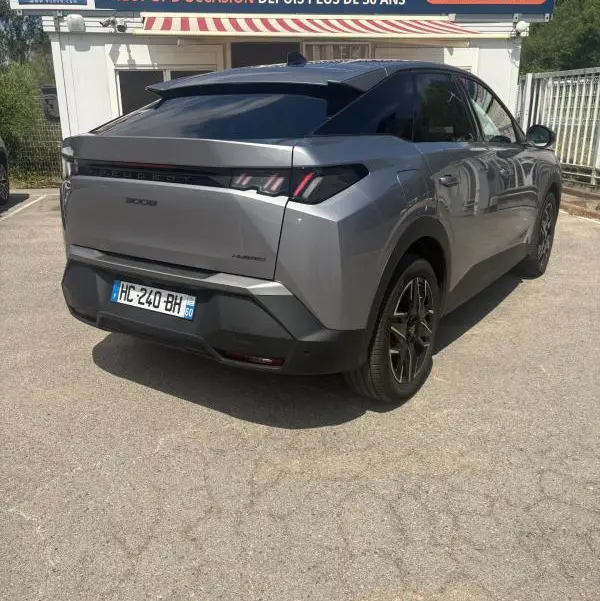 Vue 3/4 arrière droite d'un Peugeot 3008 Hybrid gris clair 2025 avec feux arrière distinctifs et toit noir.