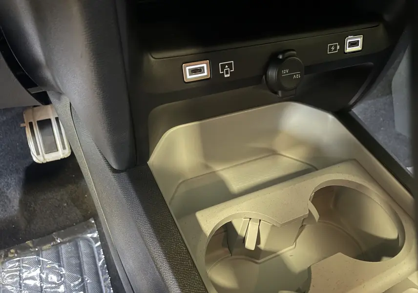 Gros plan de la console centrale du Citroën C5 Aircross hybride 2026, avec ports USB, prise 12V et porte-gobelets beige.