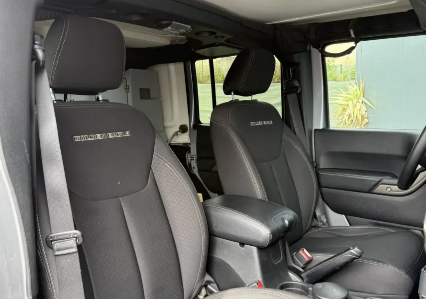 Vue intérieure avant des sièges noirs du Jeep Wrangler Golden Eagle avec accoudoir central et ceintures visibles.