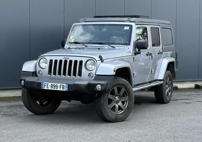 Jeep Wrangler 2.8 CRD 2019 Billet Silver en 3/4 avant droit, avec toit relevable et stickers sur capot.