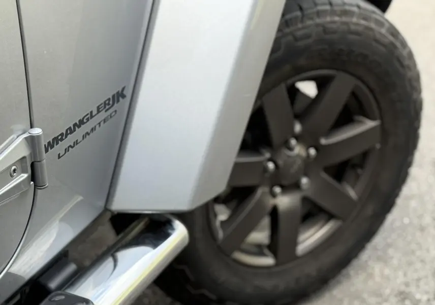 Gros plan sur la roue arrière droite et la portière argentée du Jeep Wrangler JK Unlimited avec logo visible.