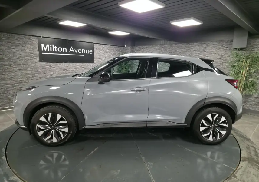 Profil côté gauche du Nissan Juke gris métallisé 2023 avec jantes bi-ton et poignées de porte couleur carrosserie.