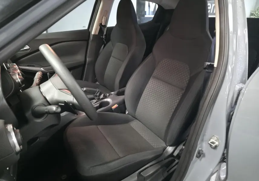 Vue intérieure côté conducteur du Nissan Juke gris 2023, mettant en valeur les sièges tissu noir et le volant réglable.