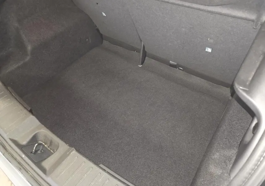 Coffre vide vu de dessus du Nissan Juke gris 2023, montrant la moquette noire et les fixations ISOFIX arrière.