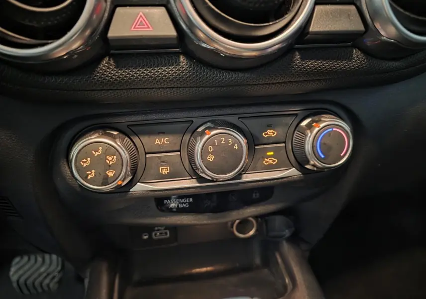 Gros plan sur les commandes de climatisation manuelle noires du Nissan Juke 2023 avec boutons éclairés orange et bleu.