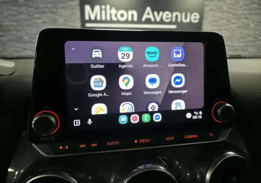 Écran tactile central du Nissan Juke 2023 affichant des applications de navigation et communication, avec commandes audio en dessous.