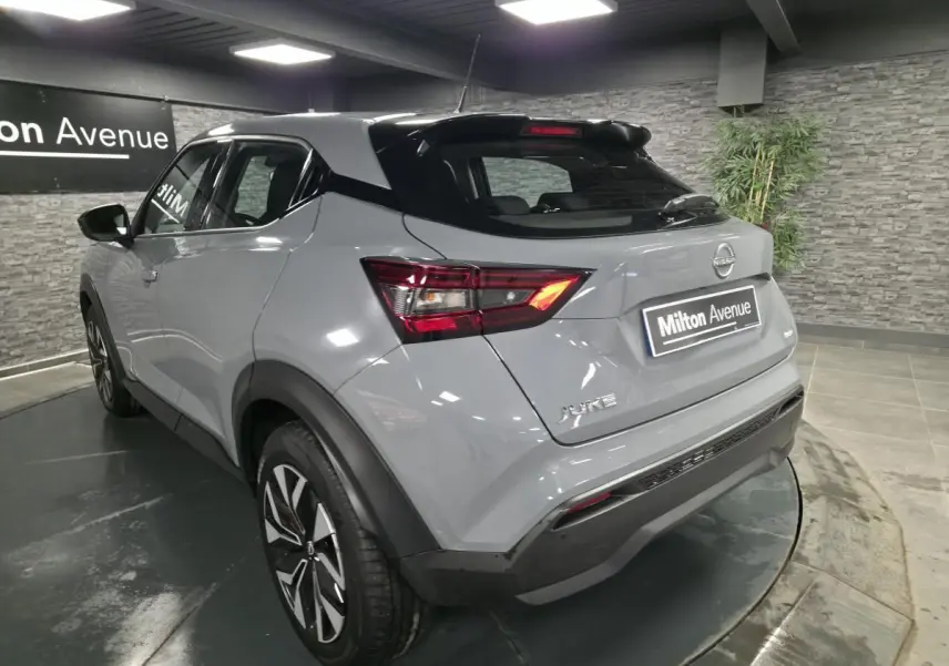 Nissan Juke gris métallisé vu en 3/4 arrière droit, avec feux LED et jantes bi-ton 17 pouces dans un showroom.