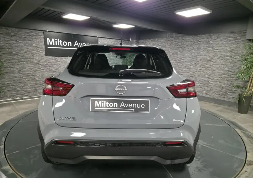 Vue arrière d'un Nissan Juke gris métallisé 2023 dans un showroom avec éclairage intérieur et panneau Milton Avenue.