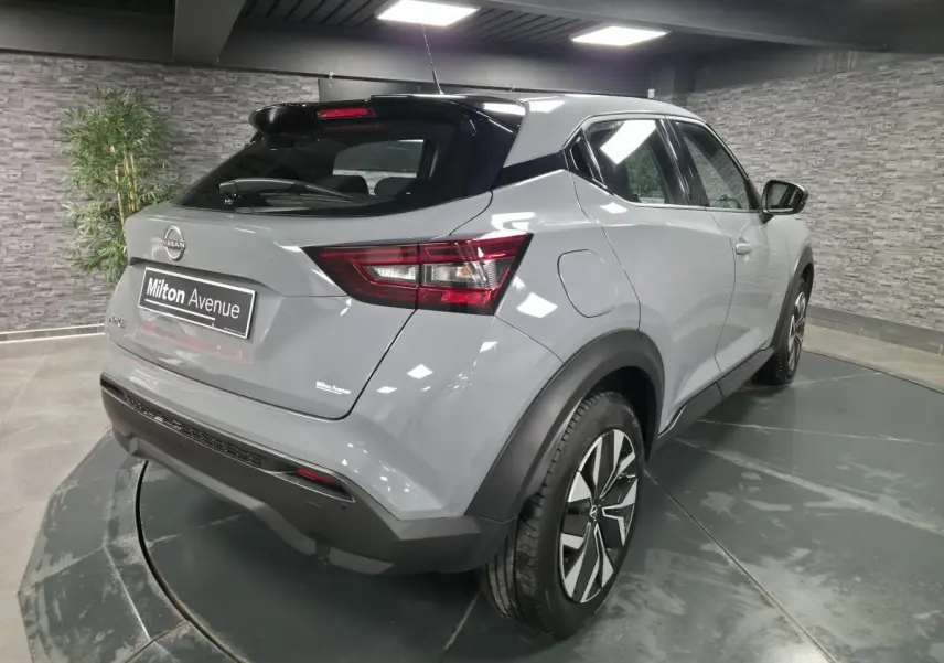 Nissan Juke gris métallisé vue 3/4 arrière droit, avec jantes bi-ton et feux arrière LED dans un showroom.