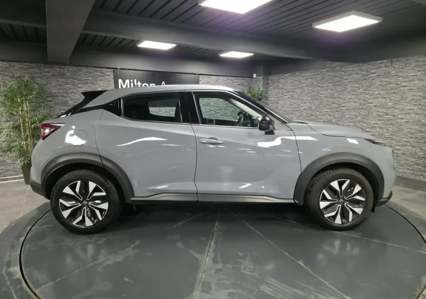 Profil côté droit du Nissan Juke gris 2023 avec jantes bi-ton et coques de rétroviseurs noires en showroom.