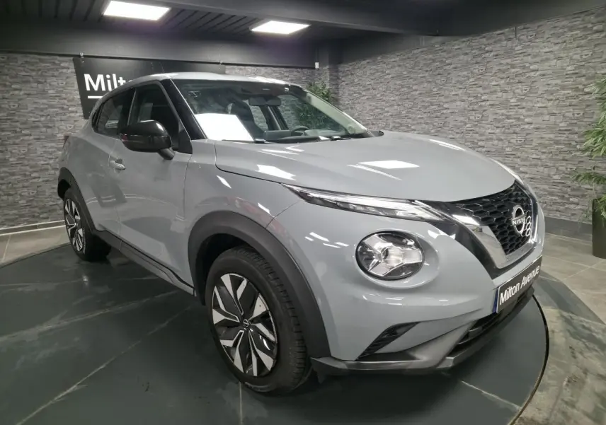 Nissan Juke gris métallisé vu en 3/4 avant droit, avec calandre noire et jantes bi-ton en intérieur showroom.