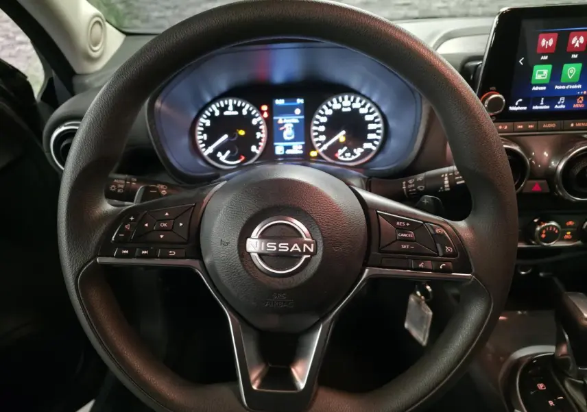 Vue intérieure centrée sur le volant noir Nissan Juke 2023 avec tableau de bord et écran tactile en arrière-plan.