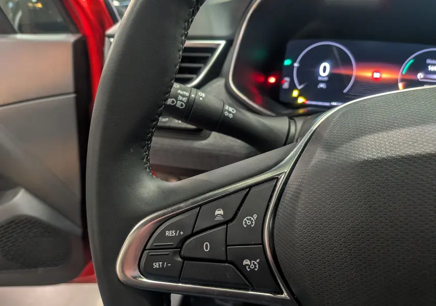 Vue rapprochée du volant côté gauche de la Renault Clio V Rouge Flamme avec commandes de régulateur et tableau de bord numérique.