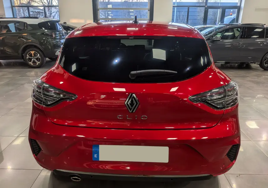 Vue arrière d'une Renault Clio V rouge flamme dans un showroom, avec feux arrière LED et logo central visible.
