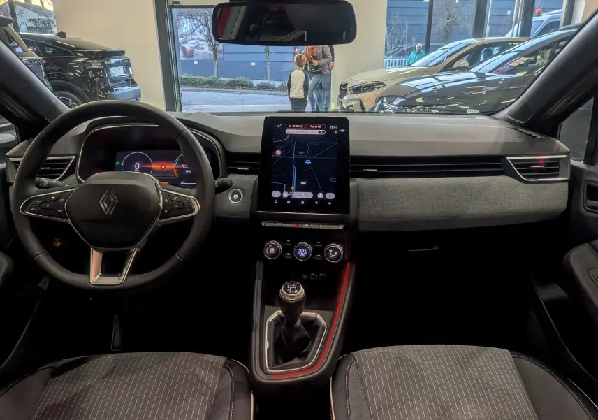 Vue intérieure avant de la Renault Clio V avec tableau de bord moderne, écran tactile vertical et levier de vitesse manuel.