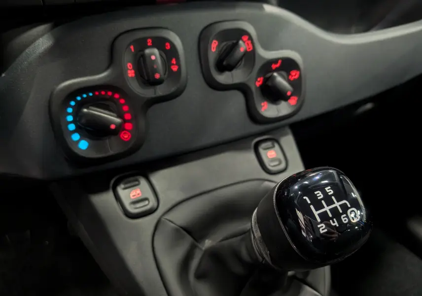 Gros plan sur le levier de vitesses manuel 6 rapports et les commandes de climatisation du tableau de bord de la Fiat Panda.