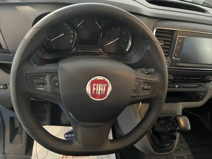 Vue rapprochée du volant FIAT noir avec logo rouge, tableau de bord et levier de vitesses manuelle visibles.