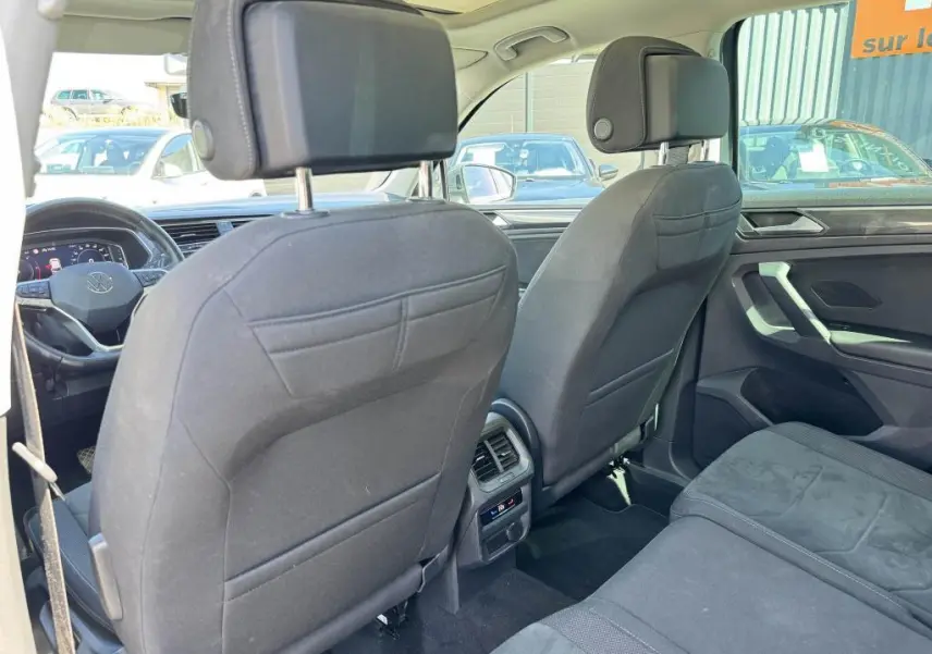 Vue intérieure arrière du Volkswagen Tiguan 2.0 TDI gris, montrant les sièges avant en tissu noir et la console centrale avec commandes climatisation.